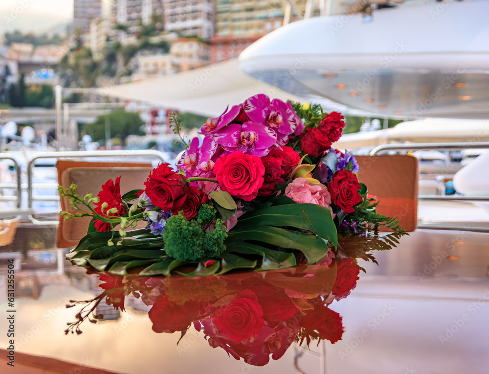 Wall mural beautiful live flower arrangement of orchids and roses on a luxury yacht with blurred monte carlo, m