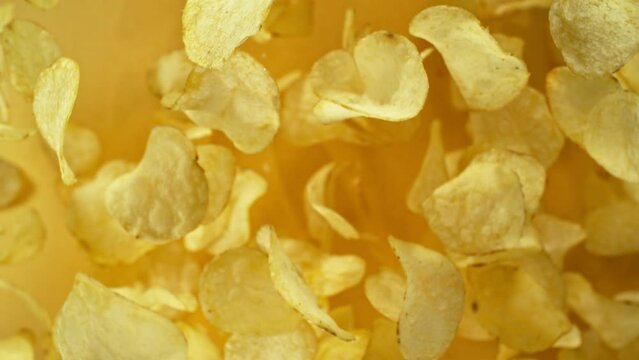 Super slow motion of flying fried potatoes chips on yellow background. Filmed on high speed cinema camera, 1000 fps. Camera placed on high speed cine bot, tracking the target. Speed ramp effect.