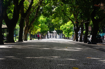Charming Scene at Republic Square: Serene Afternoon with Tree-Lined Path, Vibrant Leaves, and Family Stroll. Sunlight Illuminates the Path's End, Creating a Green and Welcoming Ambiance.