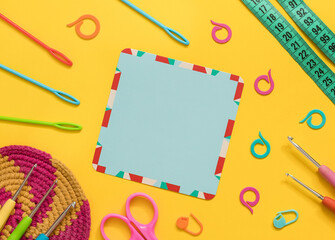 Empty blue card with crochet tools, crochet coaster on a yellow background. Top view. Copy space.