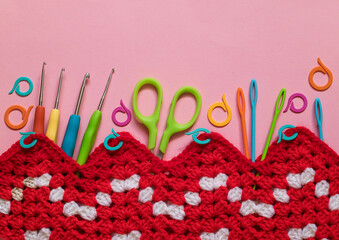 Bright crochet tools with red white crochet zig zag fabric on a pink background. Top view. Copy space.