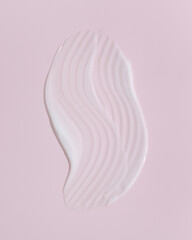 White beauty cream smear smudge on pink background. Cosmetic skincare product texture. Face cream, body lotion swipe swatch
