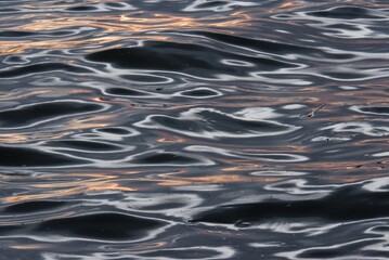 Blurred colorful light reflection on river surface with water waves in the dark night background 