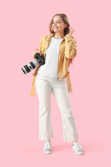 Young female photographer with professional camera on pink background