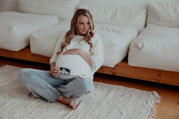 Obraz premium Pregnant blond girl holds ultrasound of baby embryo