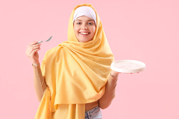 Beautiful Arabian woman with empty plate and spoon on pink background