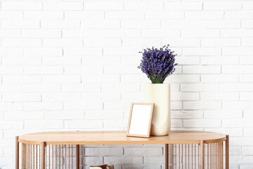 Vase with beautiful lavender flowers and blank frame on shelving unit near light brick wall in room