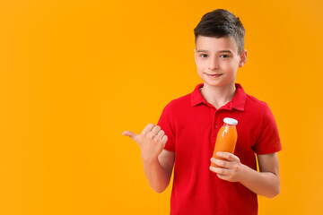 Little boy with bottle of orange juice pointing at something on color background