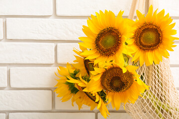 String bag with beautiful sunflowers on white brick wall