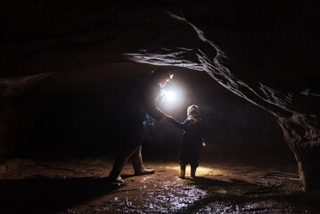 A mother and kid with a flashlight goes to the sandstone cave. - obrazy, fototapety, plakaty