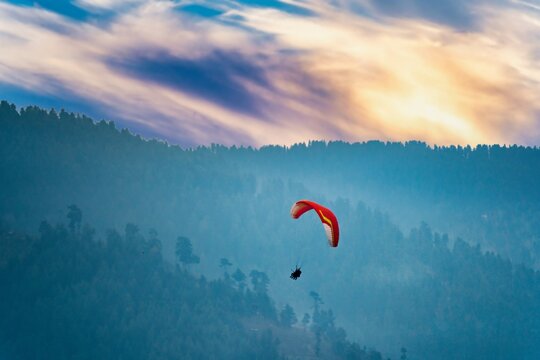 bright red para sailing being done in front of the majestic himalaya mountains in manali, bir, billing