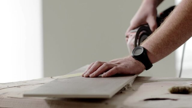 Professional tiler cutting tile with angle grinder.