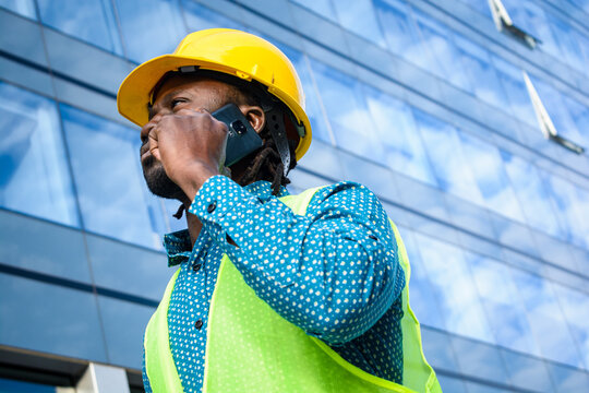 portrait of black male engineer wearing safety helmet talking on the phone and looking around.