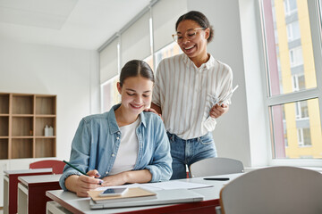 Obraz na płótnie Canvas Happy african american teacher with digital tablet standing near schoolgirl during lesson in school