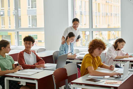 Smiling african american teacher standing near schoolgirl during lesson with devices in class