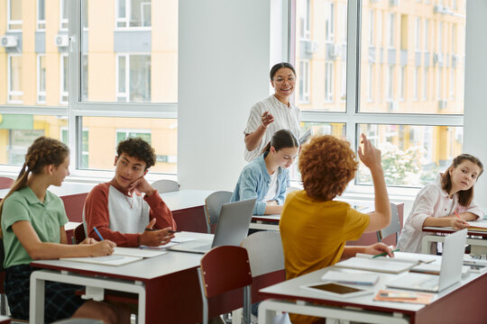 Positive african american teacher with device talking to teen pupil during lesson in classroom