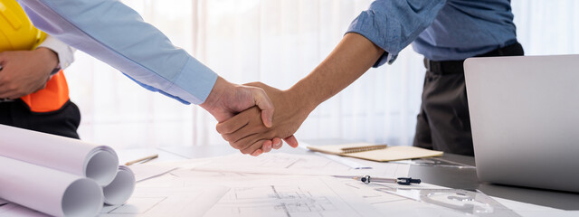 Construction engineer handshake with businessman contractor over architecture design blueprint on meeting table. Architect and engineer shake hand after successful cooperation teamwork. Insight