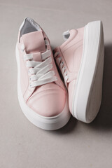 Close up details of pink leather sneakers with white sole and white laces on the floor. Casual fashion style minimalistic shoes.
