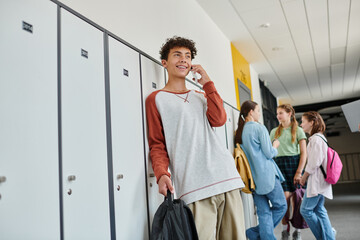 happy schoolboy with braces having phone call, talking on smartphone in school hallway, blur