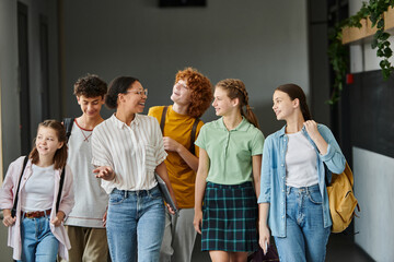 cheerful african american teacher walking with teenage students in hallway of school, education