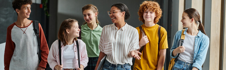 banner, happy african american woman walking with teen students in school hallway, teacher and kids © LIGHTFIELD STUDIOS