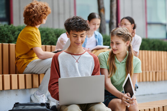 back to school, happy boy and girl using gadgets near school, teenage students outdoors, e-study - Powered by Adobe