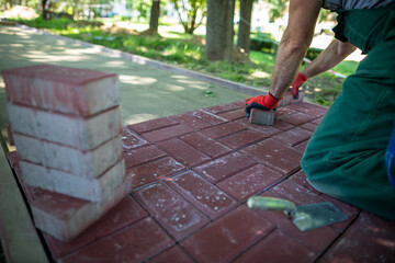 An experienced paving worker kneels while laying paving stones.