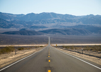 a desert road leads to the mountains of Death Valley National Park, California, USA