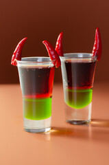 Layered drink shot prepared with vodka, green liquor, grenadine and lemon juice decorated with bird eye chillies in the shape of horns
