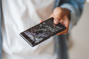 Male hand  holding broken mobile phone with cracked screen, selective focus. Technology, service,...