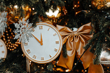 Christmas clock hanging on the Christmas tree with golden bow. New Year magic details. Festive...