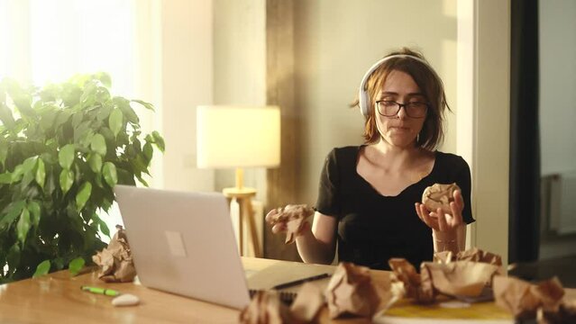 Portrait of funny young woman juggles crumpled papers with failed ideas while take a break at home Tired female with positive reaction to creative block or lack of inspiration indoors