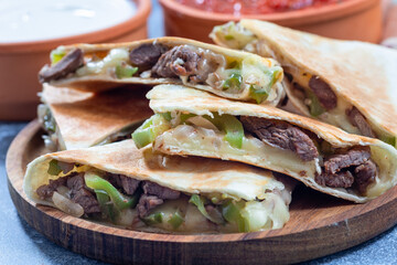 Fajita quesadilla with pieces of beef steak, green bell pepper, onion and cheese, on a wooden plate