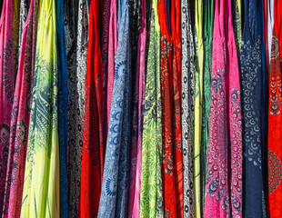 Multicolored colorful scarves hang on the counter under sunlight.
