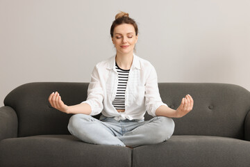 Fototapeta na wymiar Woman meditating on sofa near light grey wall. Harmony and zen