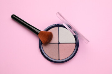 Colorful contouring palette with brush on pale pink background, top view. Professional cosmetic product