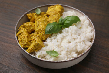 Delicious rice and chicken with curry sauce on wooden table, closeup