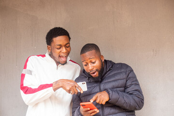 young african men standing outside excited and delighted while using there smart phone