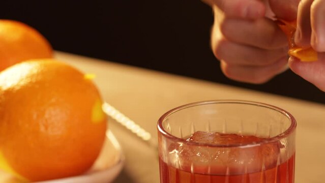 Zest orange peel into a Negroni cocktail