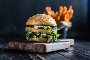 Close-up of burger with salmon patty, lettuce and sweet potato fries in the background