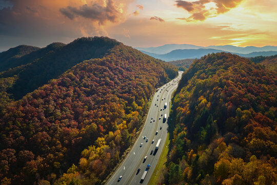Aerial view of I-40 freeway in North Carolina heading to Asheville through Appalachian mountains in golden fall with moving trucks and cars. Interstate transportation concept