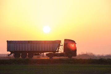Fototapeta Semi-truck with tipping cargo trailer transporting sand from quarry driving on highway hauling goods in evening. Delivery transportation and logistics concept obraz