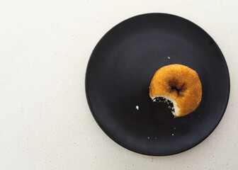 Flat lay of a donut with a bite taken out on a black plate