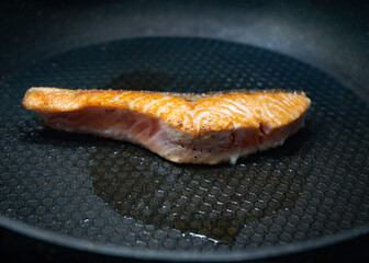 Rare salmon fillet cooking in a black pan