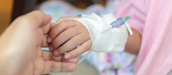 Mother holding child hand with saline IV solution in hospital