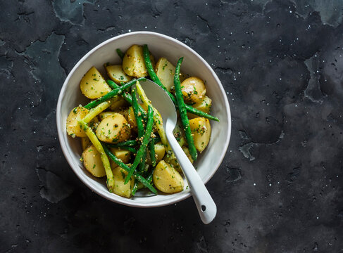 Vegetarian salad with new potatoes, green string beans and lemon-mustard dressing on a dark background, top view