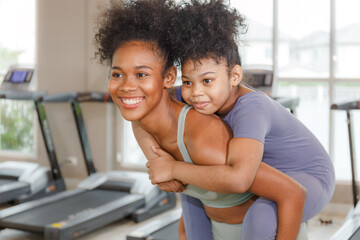 woman with daughter Riding on mom's back after healthy yoga workout in gym, smiling.