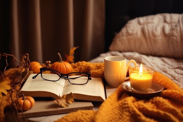 Burning candle, pumpkin decor and mug of lemon tea, Open book with eyeglasses and cozy sweater on bed, Autumn cozy home and hygge