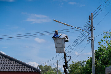 Electrician standing in the basket of a car fixing a lamp at a power pole - 631381732