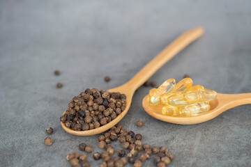 Black pepper granules in wooden spoon with black pepper capsules The piperine found in black pepper has anti-obesity properties. and burn fat well. - 631381783